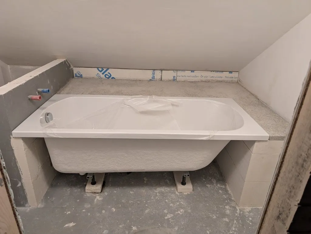 Test-fitting the bathtub. The legs are adjustable, making it easy to level the bathtub, but they were too short, so the bathtub rests on aerated concrete block (and is additionally supported around its edge by the wall enclosure).