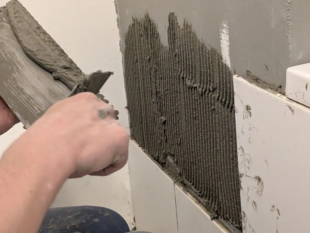 Applying tile adhesive to the bathtub walls. A notched trowel is used to create the neat line pattern—this makes for a better bond when the tile is pressed into the adhesive, and makes it easy to spread a consistent thickness adhesive.