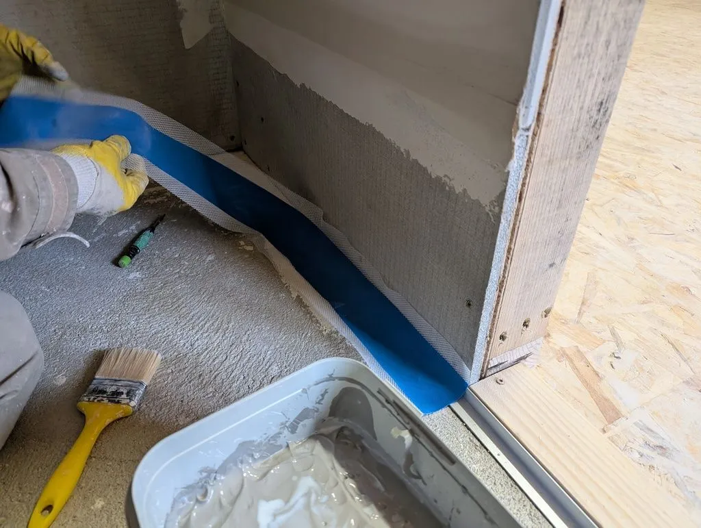 An elastic waterproofing tape is applied over all corners; the waterproofing compound is then applied over the tape.