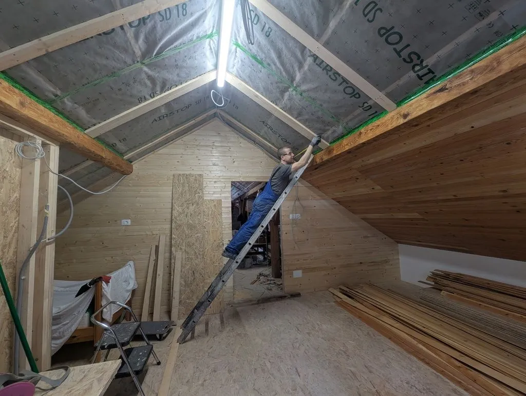 Our not-quite-OSHA-approved setup for reaching the start of the top sector. (I didn't lean the ladder higher up the ceiling at a more comfortable angle because it would risk puncturing the vapor barrier, which has only soft insulation underneath. Although I'm not sure why we didn't use a self-supporting A-frame ladder; perhaps we were playing around intentionally.)