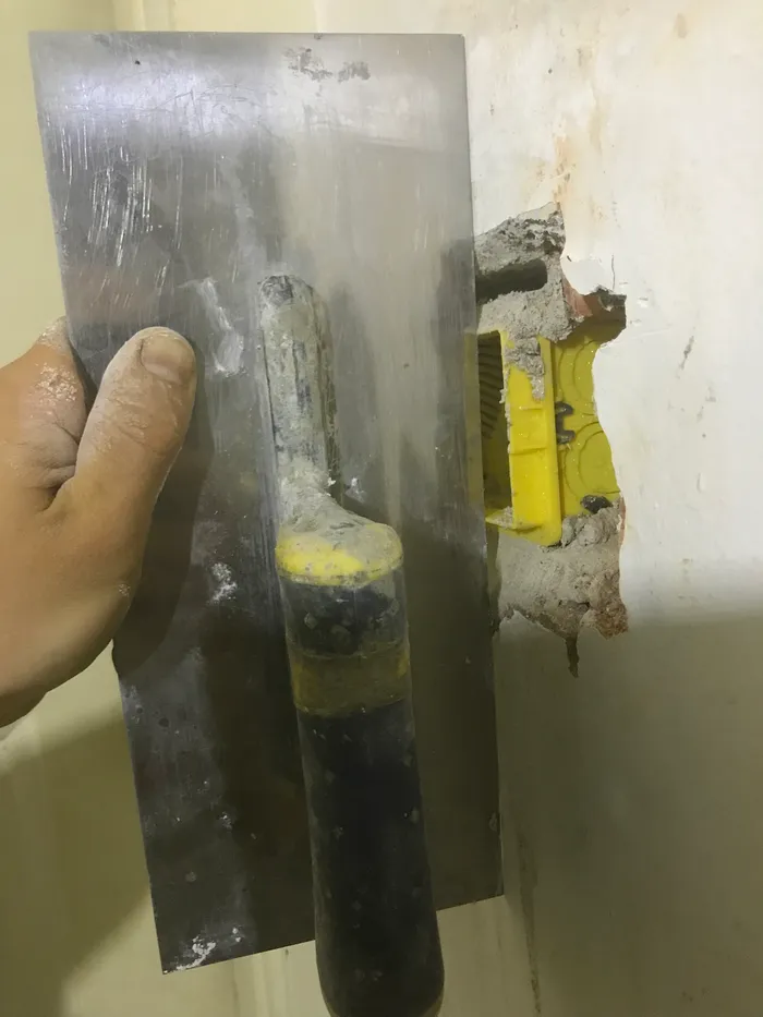 Using a straight-edge to ensure the face of the new box is flush with the plane of the existing wall.